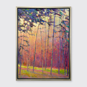 A red, orange and blue abstract tree landscape print in a silver floater frame hangs on a white wall.