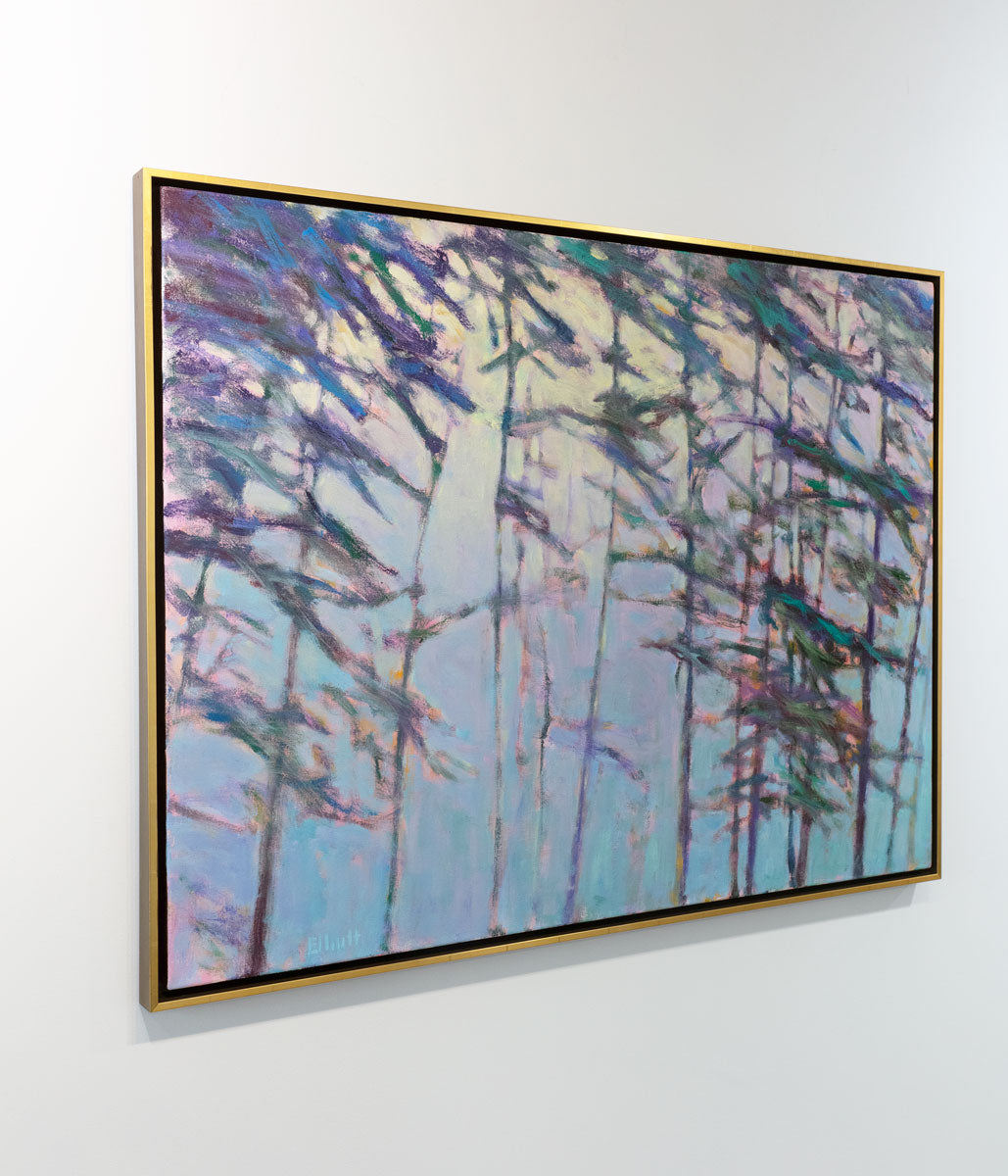 An impressionistic landscape painting by Ken Elliott of trees with blue and purple leaves in a gold floater frame hangs on a white wall in the gallery with a view from the left.