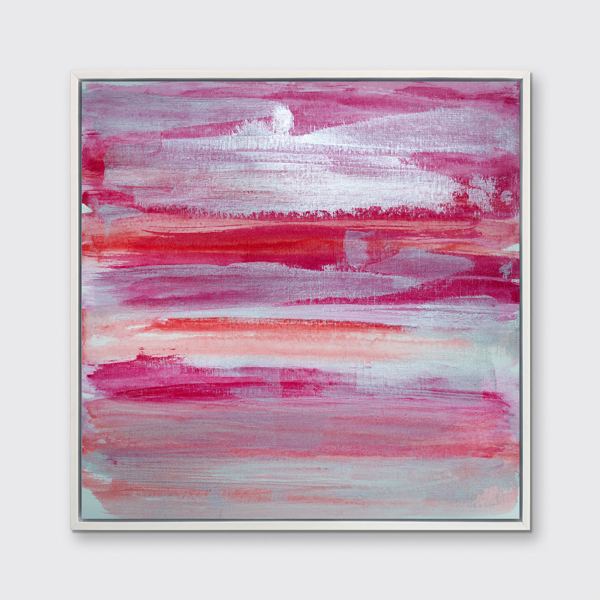 A pink, white, silver and red abstract print in a white floater frame hangs on a white wall.