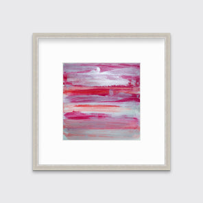 A pink, white, silver and red abstract print in a silver frame with a mat hangs on a white wall.