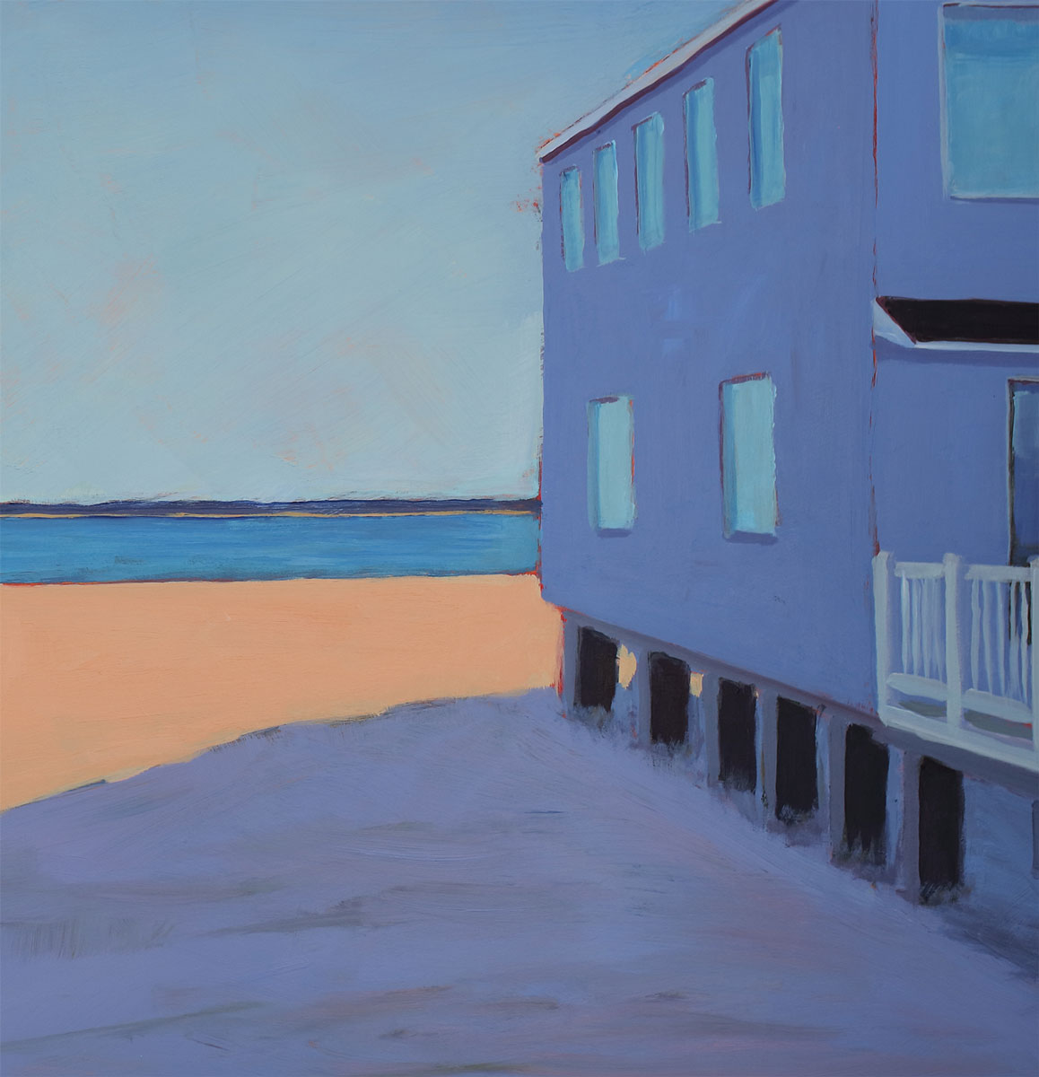 Close up view of the side of a purple beach house, showing the dark cerulean water and the sunlit beach.