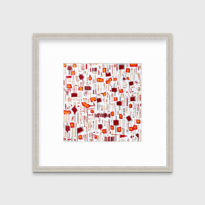 A red, white and orange abstract print in a silver frame with a mat hangs on a white wall.