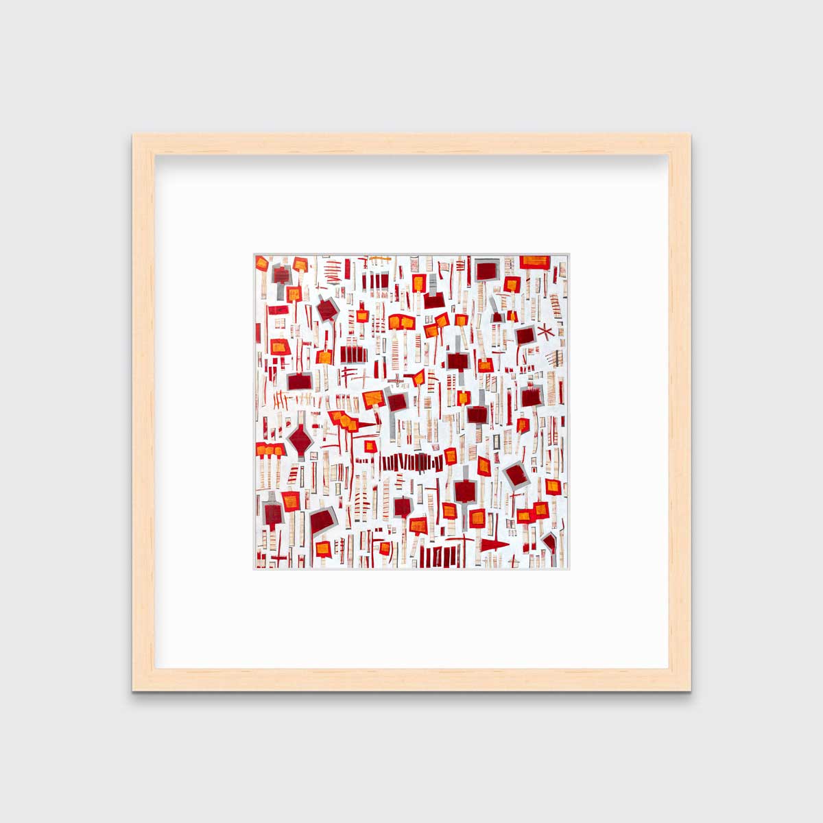 A red, white and orange abstract print in a natural wood frame with a mat hangs on a white wall.