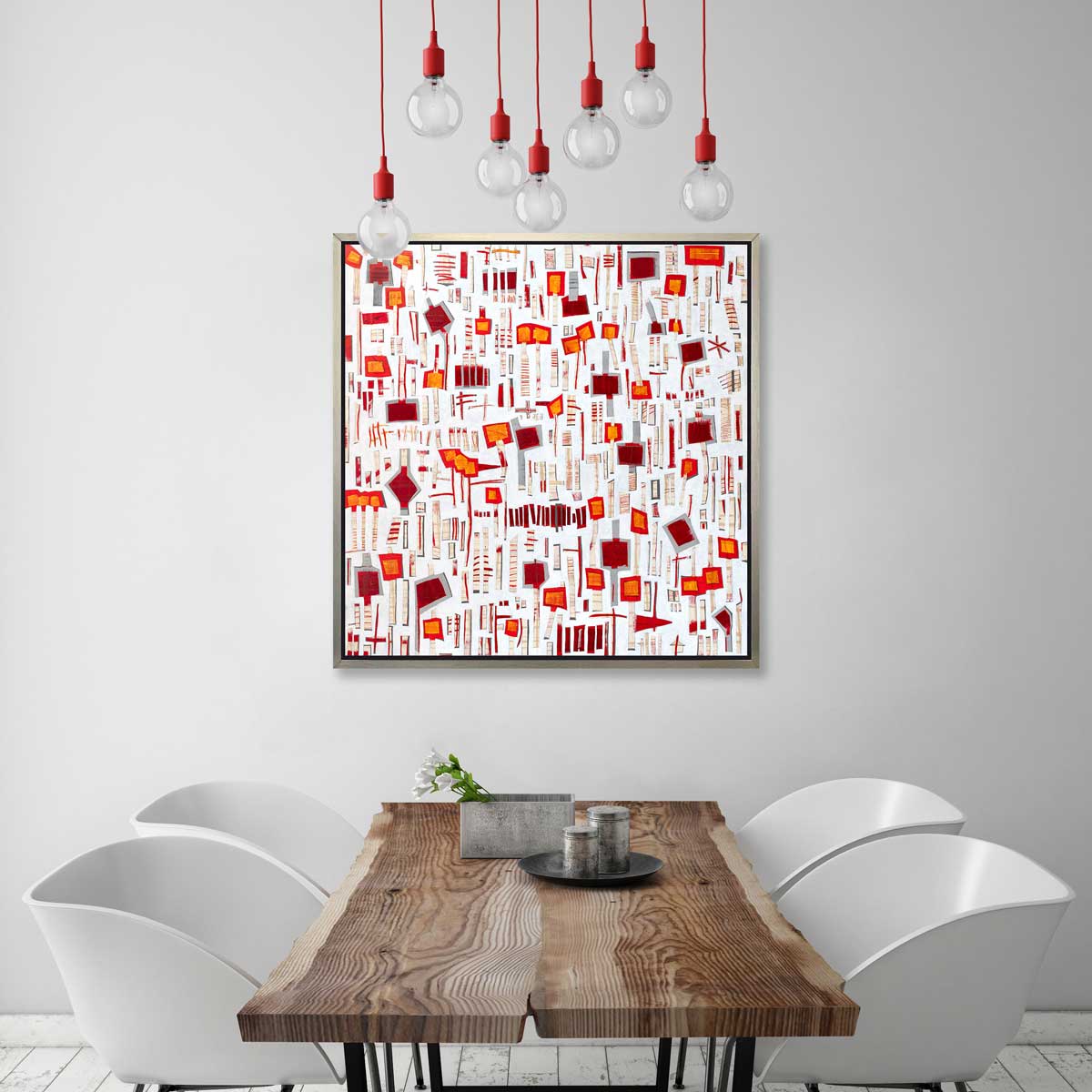 A red, white and orange abstract print in a silver floater frame hangs on a white wall above a live edge wood table and four modern white chairs.