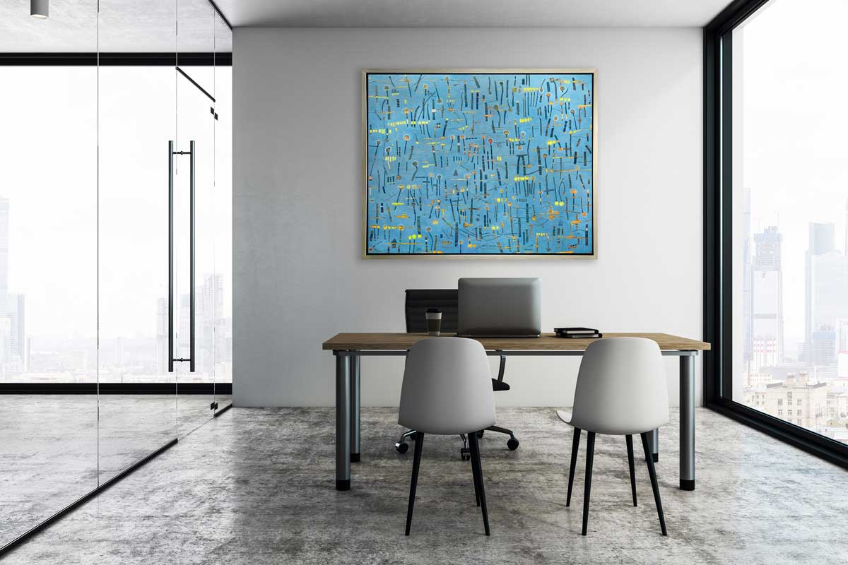A blue, yellow and orange abstract print in a silver floater frame hangs on a white wall above a wood desk, a black chair and two grey chairs.