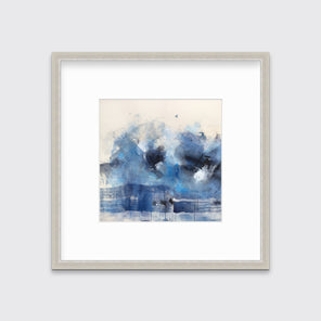 A blue, beige, white and black abstract print in a silver frame with a mat hangs on a white wall.