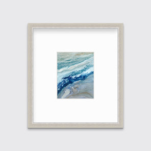 A blue, teal, gold and white abstract print in a silver frame with a mat hangs on a white wall.