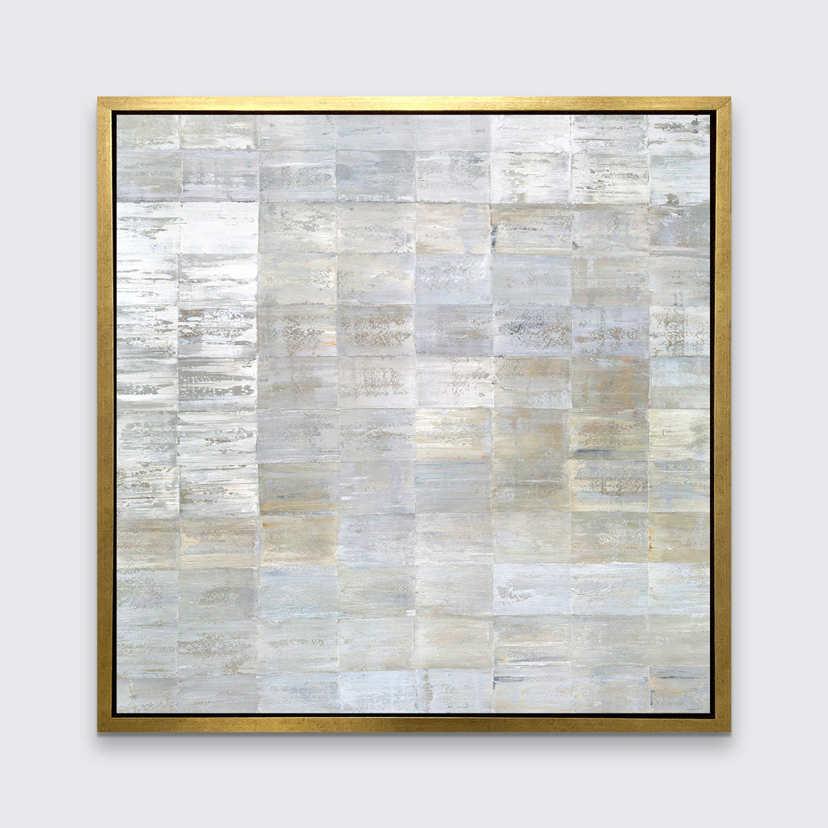 A grey, silver and light gold abstract geometric print in a gold floater frame hangs on a white wall.