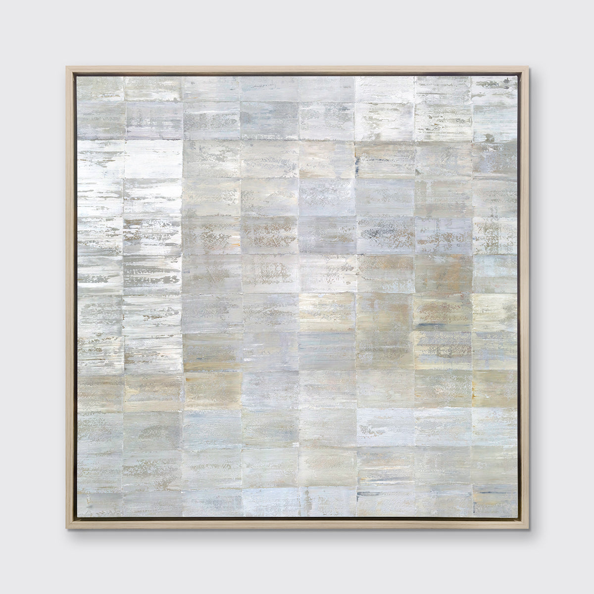 A grey, silver and light gold abstract geometric print in a white oak wood floater frame hangs on a white wall.