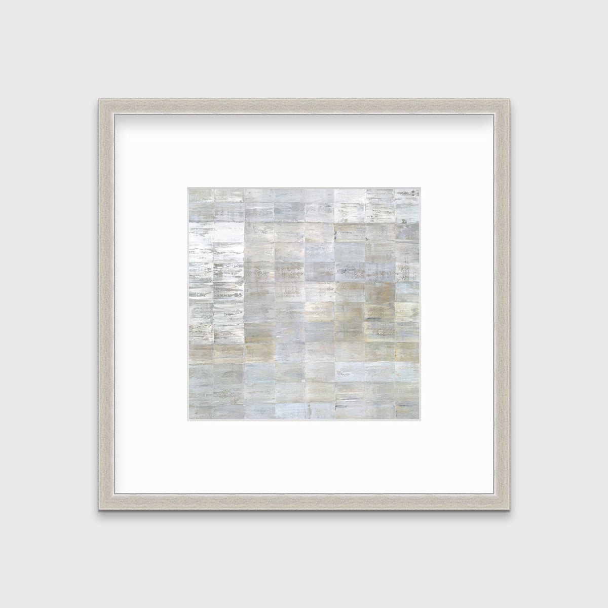 A grey, silver and light gold abstract geometric print in a silver frame with a mat hangs on a white wall.