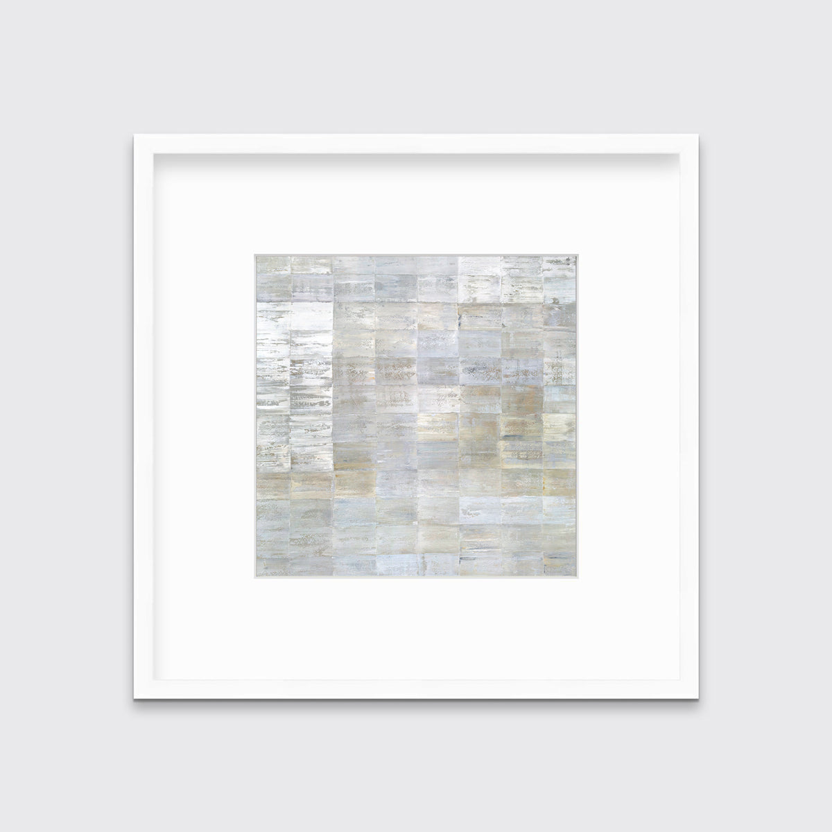 A grey, silver and light gold abstract geometric print in a white frame with a mat hangs on a white wall.