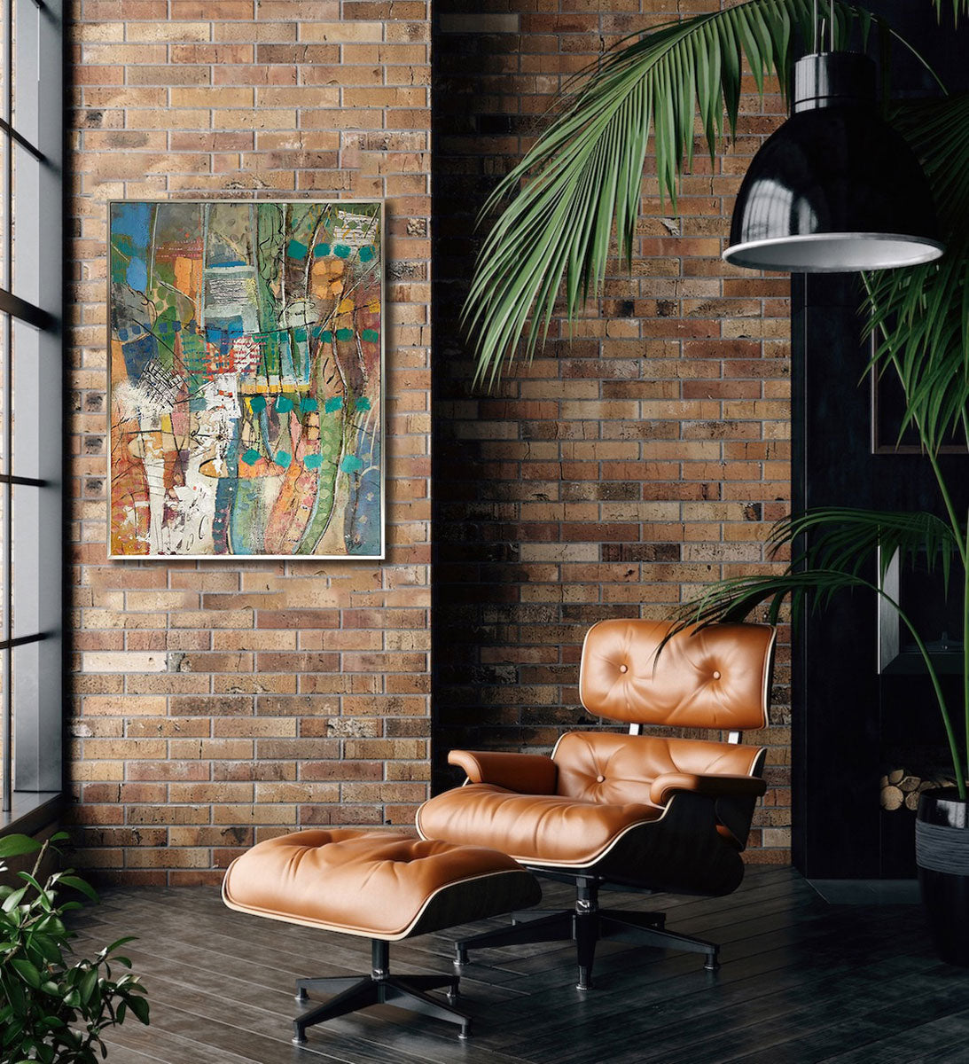 A multicolored abstract print, framed in a gold floater frame, hangs on a brick wall next to a window above a leather reclining chair and potted plants. 