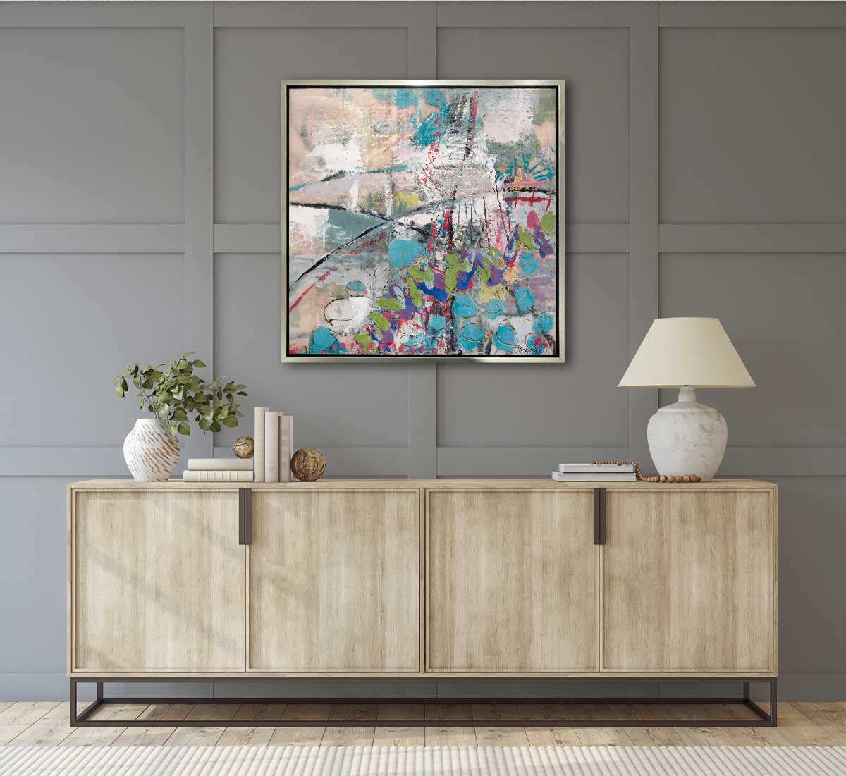 A print of Linda Bigness' painting, Marks of Passion, matted in a warm silver floater frame, hanging on a grey wall above a natural wood console with a lamp and decorative books. 