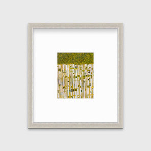 A green, yellow and white abstract print in a silver frame with a mat hangs on a white wall.