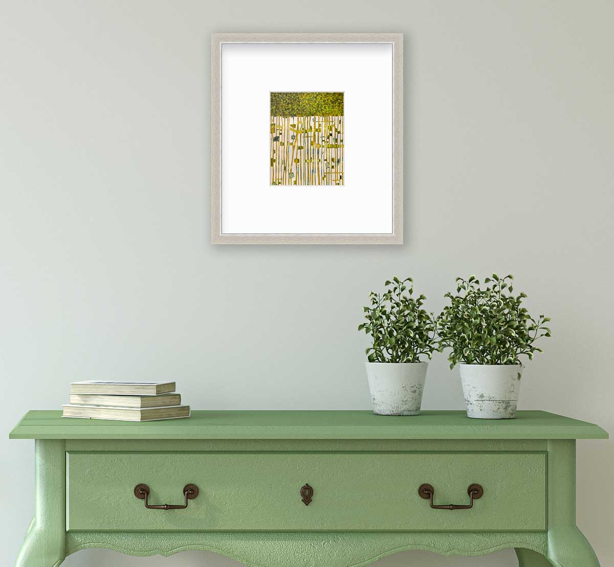 A green, yellow and white abstract print in a silver frame with a mat hangs on a white wall above a green console table with a stack of books and two potted plants.