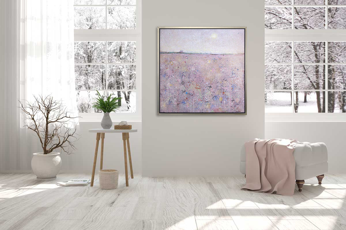 A pink abstract landscape print in a silver floater frame hangs on a white wall above a white ottoman with a pink blanket, a white side table with a vase of greenery and a box of tissues and a potted floor plant.