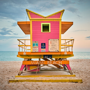 A photograph of a pink, yellow and orange lifeguard stand looking out over the ocean. 