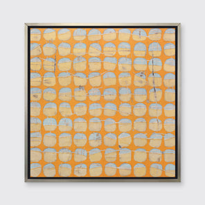 An orange and light blue abstract circle print in a silver floater frame hangs on a white wall.