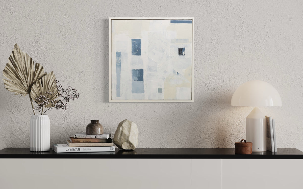 A white and beige abstract painting with blue and black rectangular forms is hung above a console table. Wired and ready to hang.