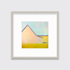 A light blue, coral and deep yellow landscape print of a barn in a silver frame with a mat hangs on a white wall.