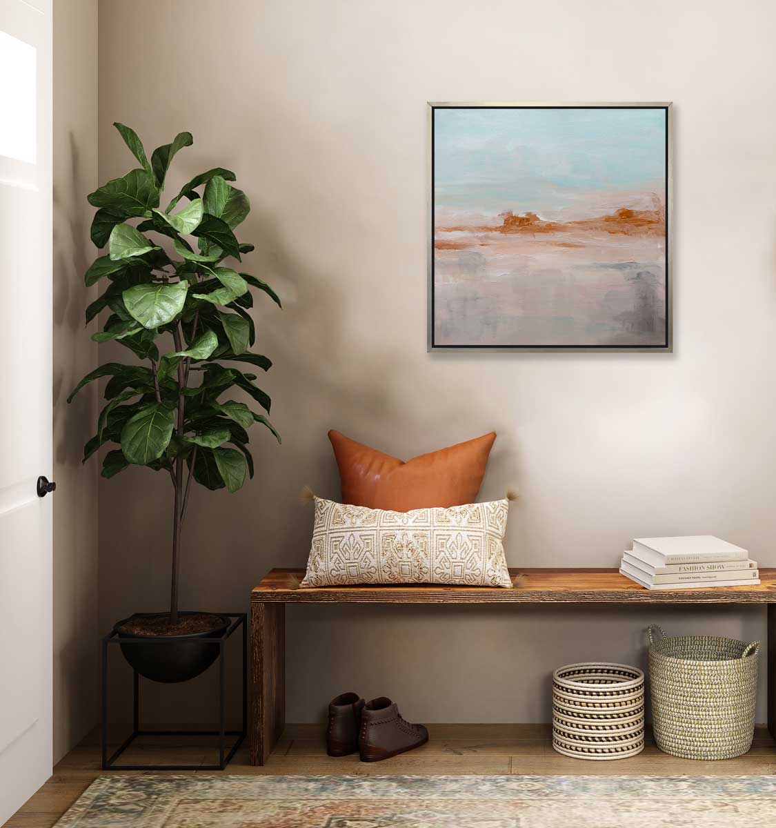A teal, copper and dusty pink abstract print in a silver floater frame hangs on a white wall above a natural wood bench with copper pillows and books, two woven baskets, a pair of low brown boots and a potted floor plant.