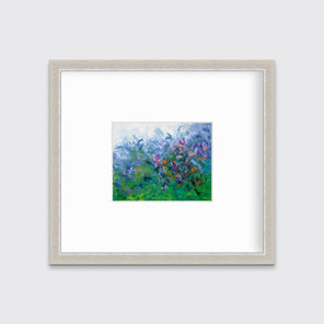 A multicolored abstract floral print in a silver frame with a mat hangs on a white wall.