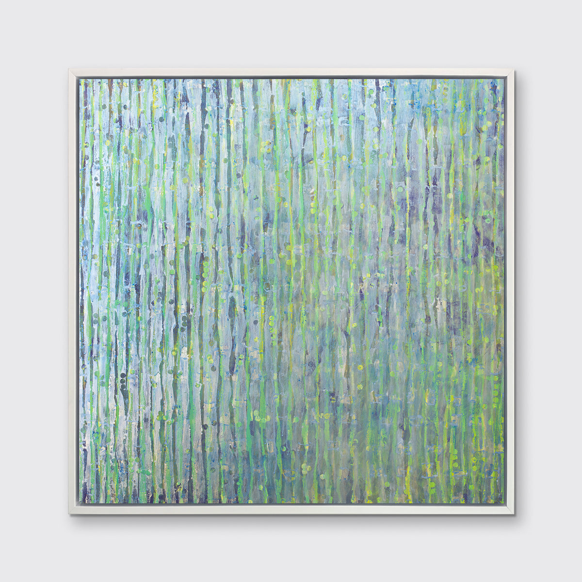 A green, blue and yellow abstract print in a white floater frame hangs on a white wall.