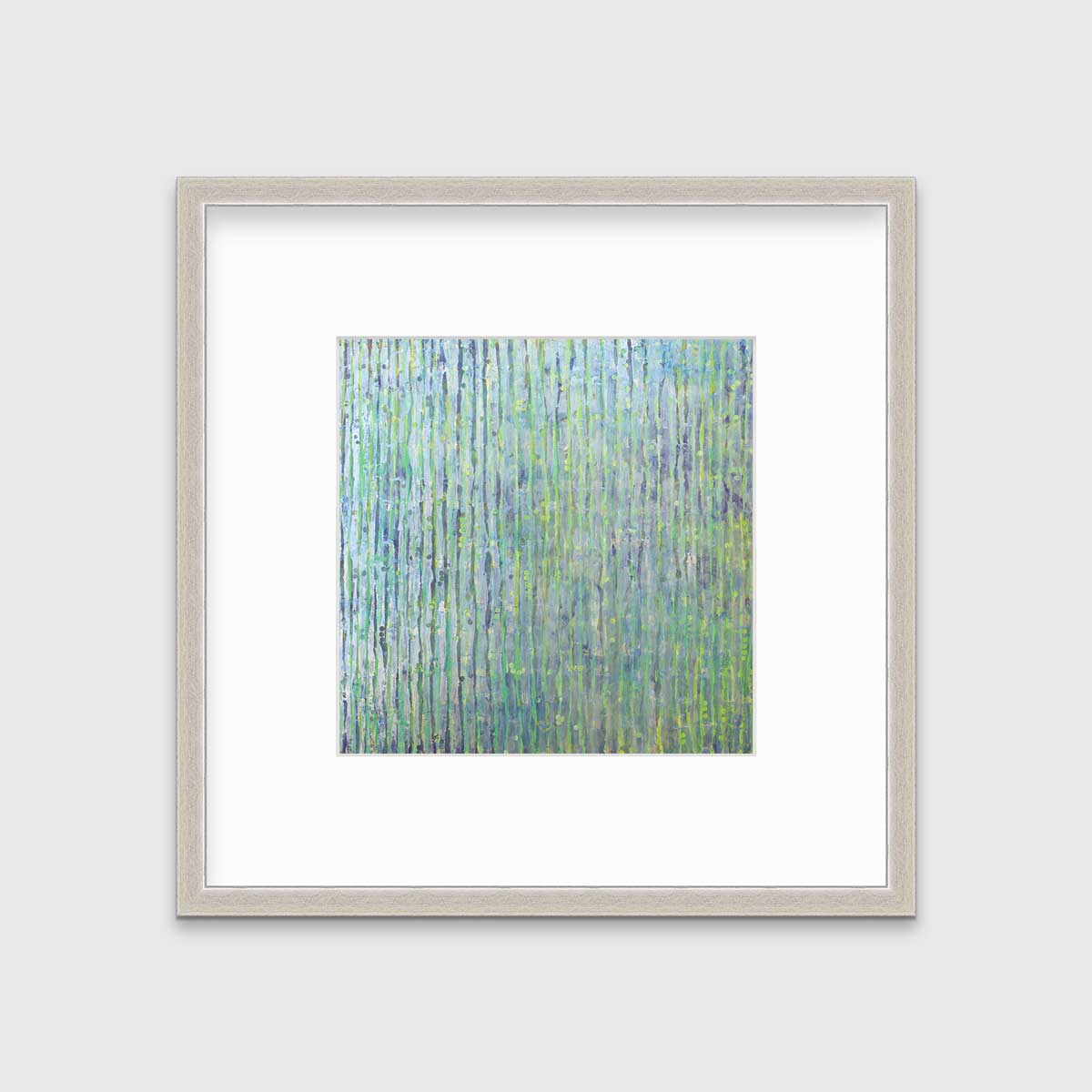 A green, blue and yellow abstract print in a silver frame with a mat hangs on a white wall.