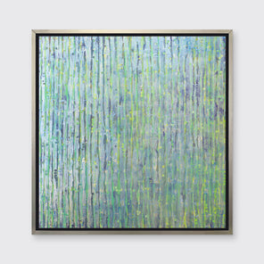 A green, blue and yellow abstract print in a silver floater frame hangs on a white wall.