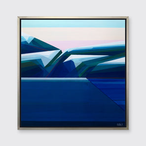 A tonal blue, green and light beige geometric abstract landscape print in a silver floater frame hangs on a white wall.