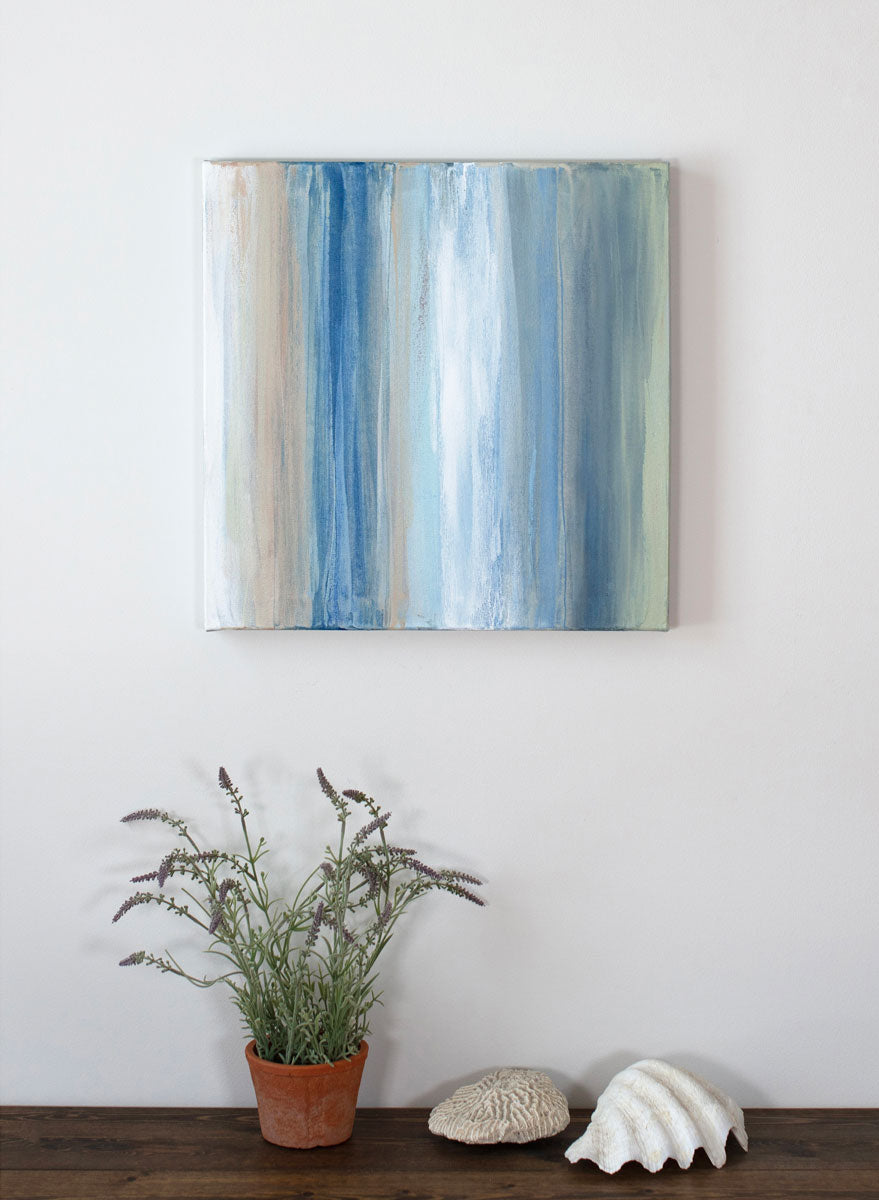 An original painting painted in tan, blue, white, and green streaks hangs above a shelf decorated with lavender and seashells. Wired and ready to hang.