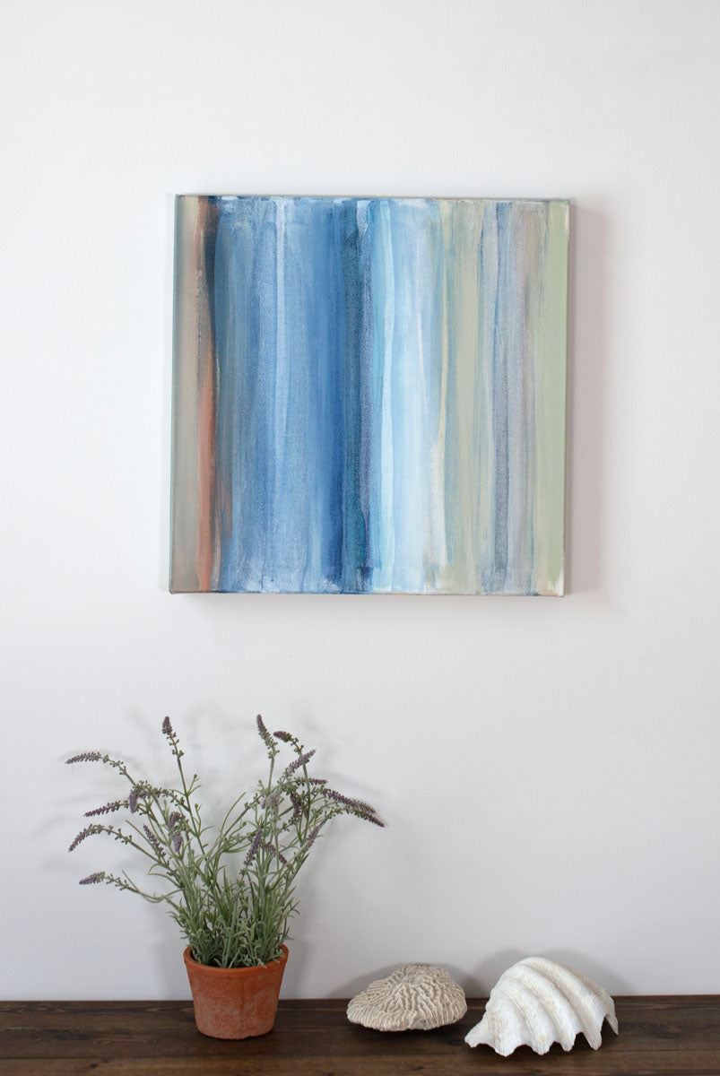 A tan canvas decorated with blue, white, and green streaks hangs above a shelf decorated with lavender and seashells. Wired and ready to hang.