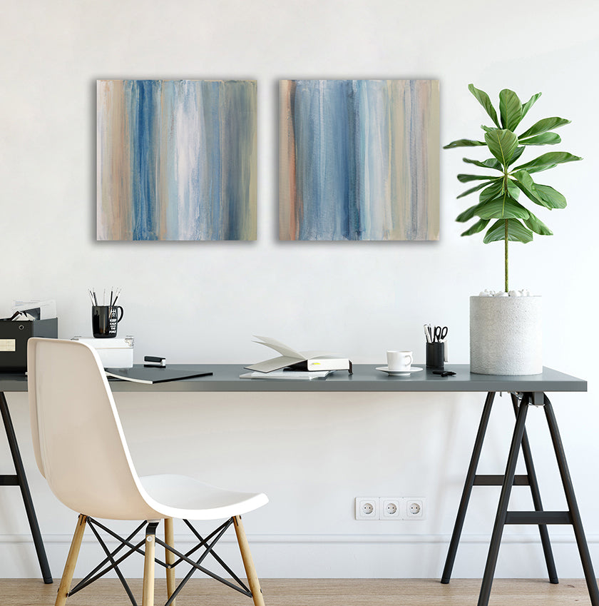 A pair of paintings painted with blue, white, tan and green streaks hangs above a black desk with a plant books, pencils and white chair.  Wired and ready to hang.