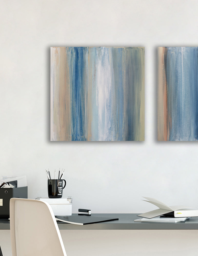 One of a pair of paintings painted with blue, white, tan and green streaks hangs above a black desk with a plant books, pencils and white chair. Wired and ready to hang.