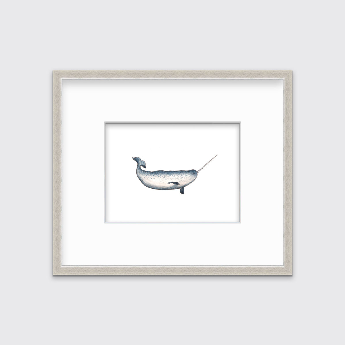 A blue and white narwhal print in a silver frame with a mat hangs on a white wall.