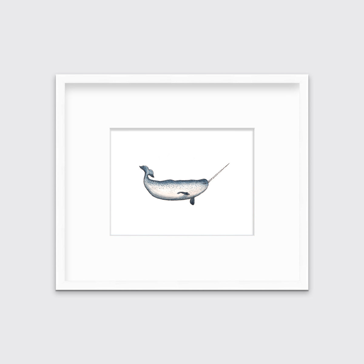 A blue and white narwhal print in a white frame with a mat hangs on a white wall.