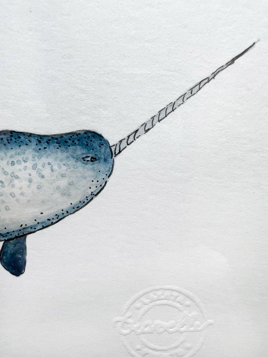 A close up view of the face of the narwhal with a long spiral horn and the artist's stamp.