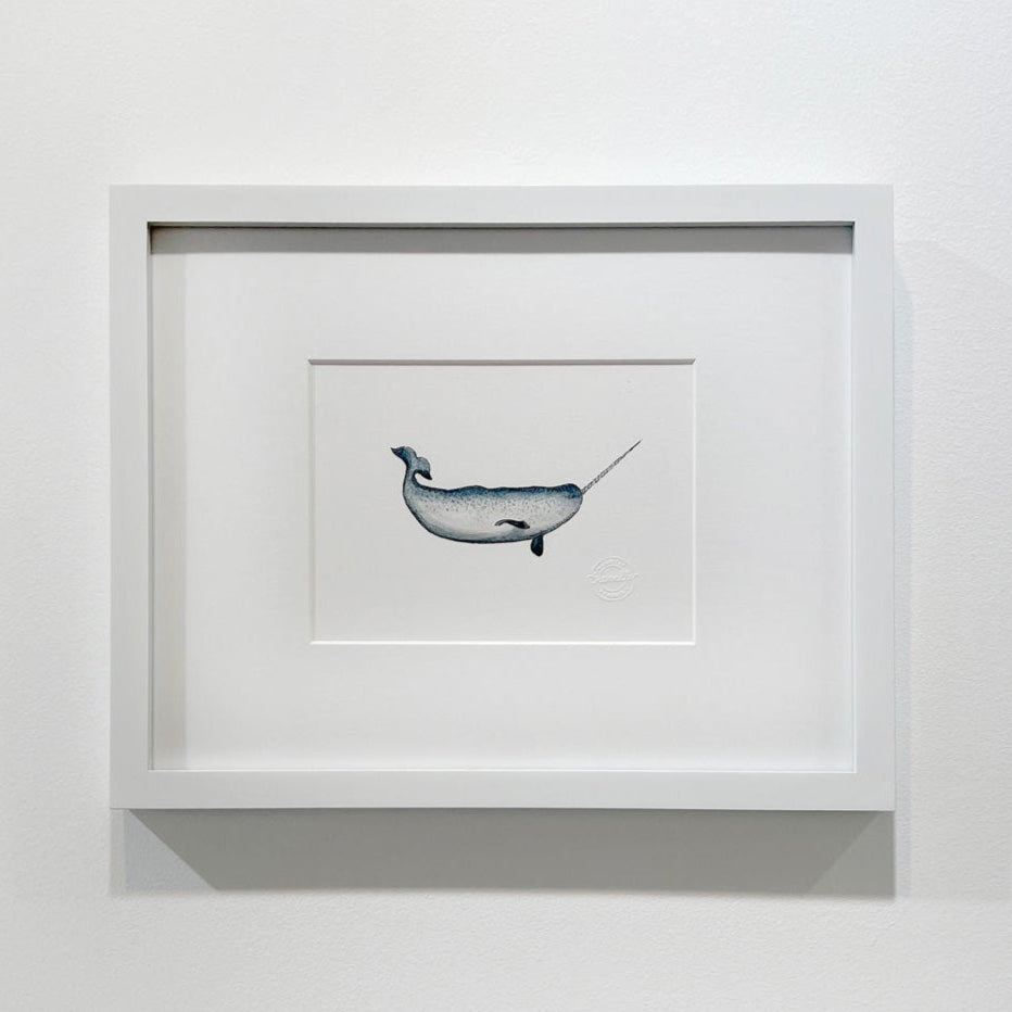 A blue, white and black illustration drawing of a narwhal sea creature in a white frame with a mat hangs on a white wall.