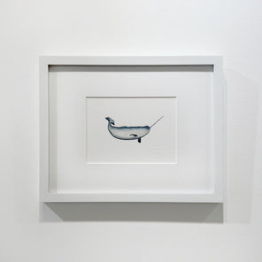 A blue, white and black illustration drawing of a narwhal sea creature in a white frame with a mat hangs on a white wall.