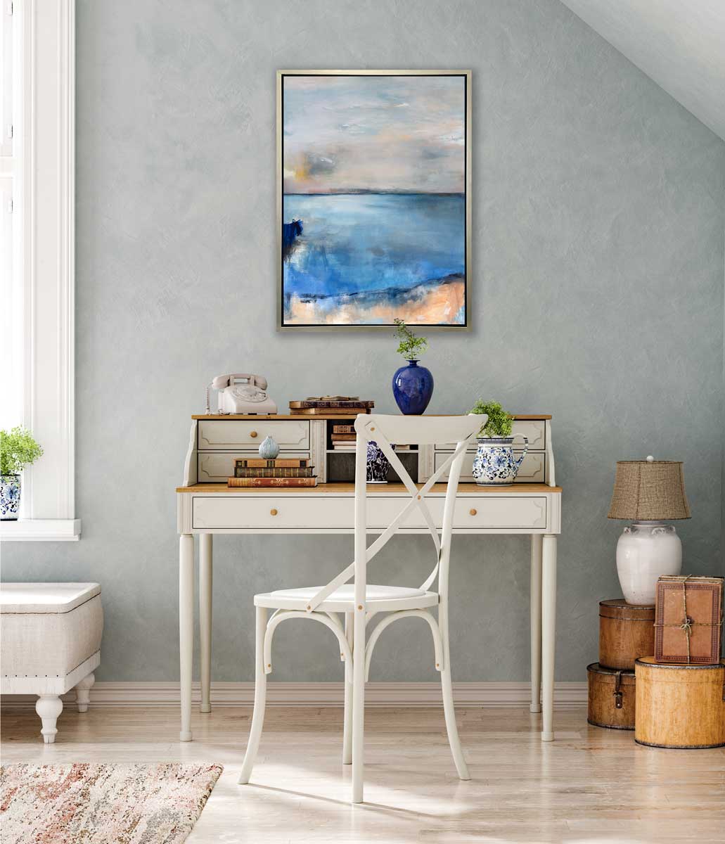 A blue and grey abstract print in a silver floater frame hangs on a light teal wall above a two-tiered white desk and a white chair.