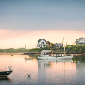 A panoramic photograph of a harbor at sunset in Block Island, Rhode Island with boats docked in the water and houses in the distance.