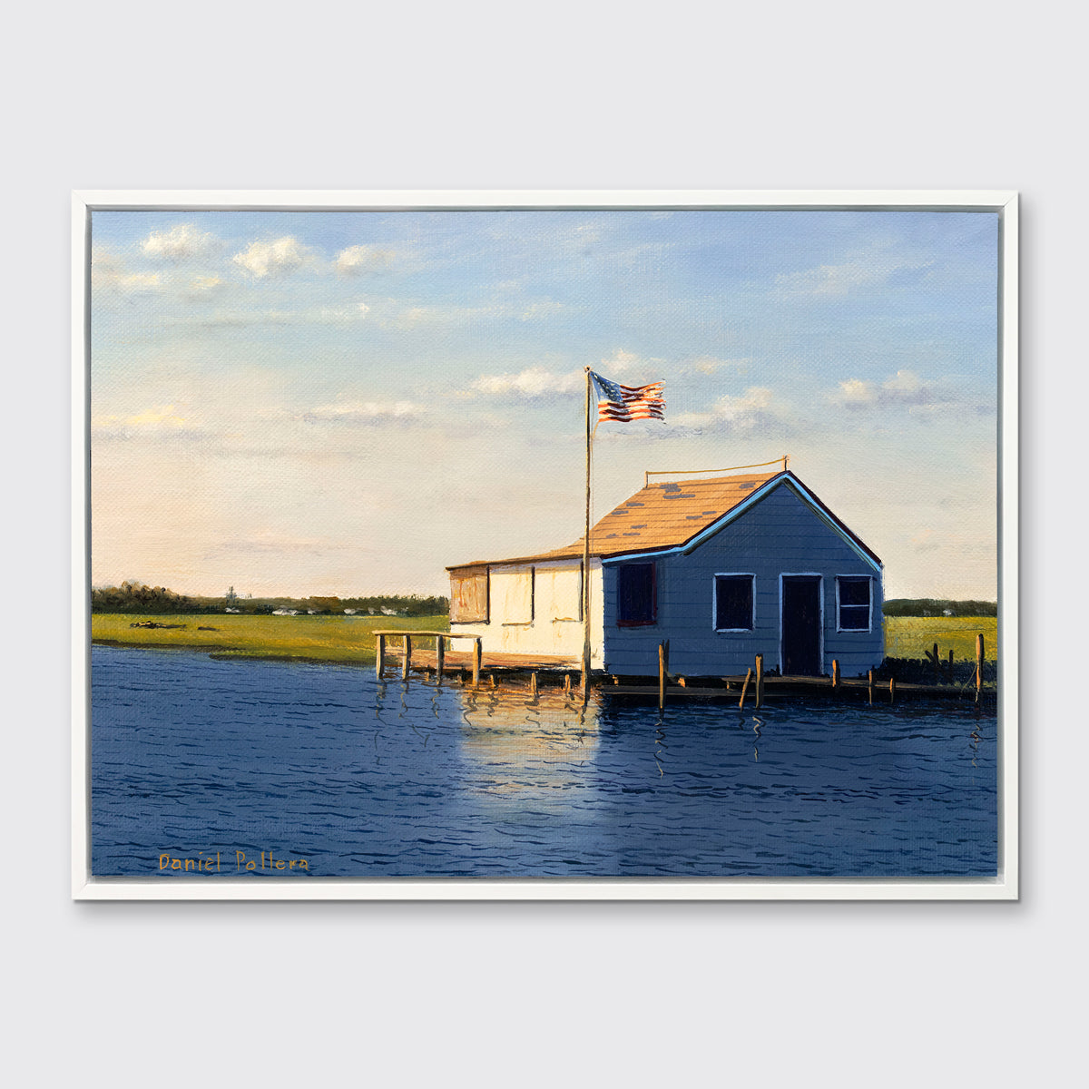 A blue, beige and green contemporary seascape print with a bay house in a white floater frame hangs on a white wall.