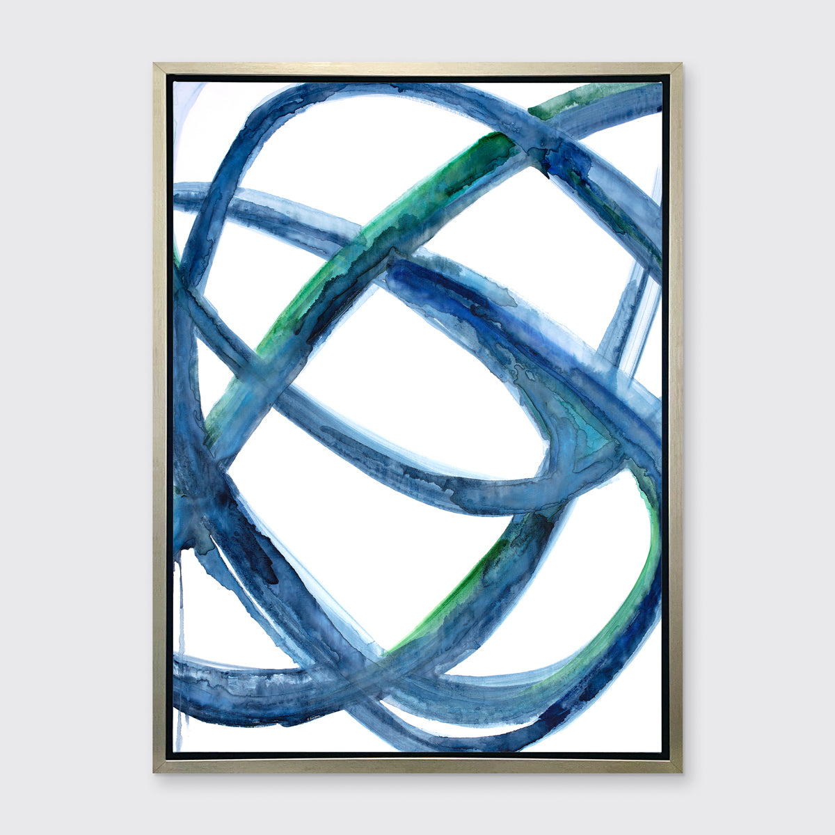 A blue, green, and white abstract print framed in a warm silver frame hangs on a light grey wall.