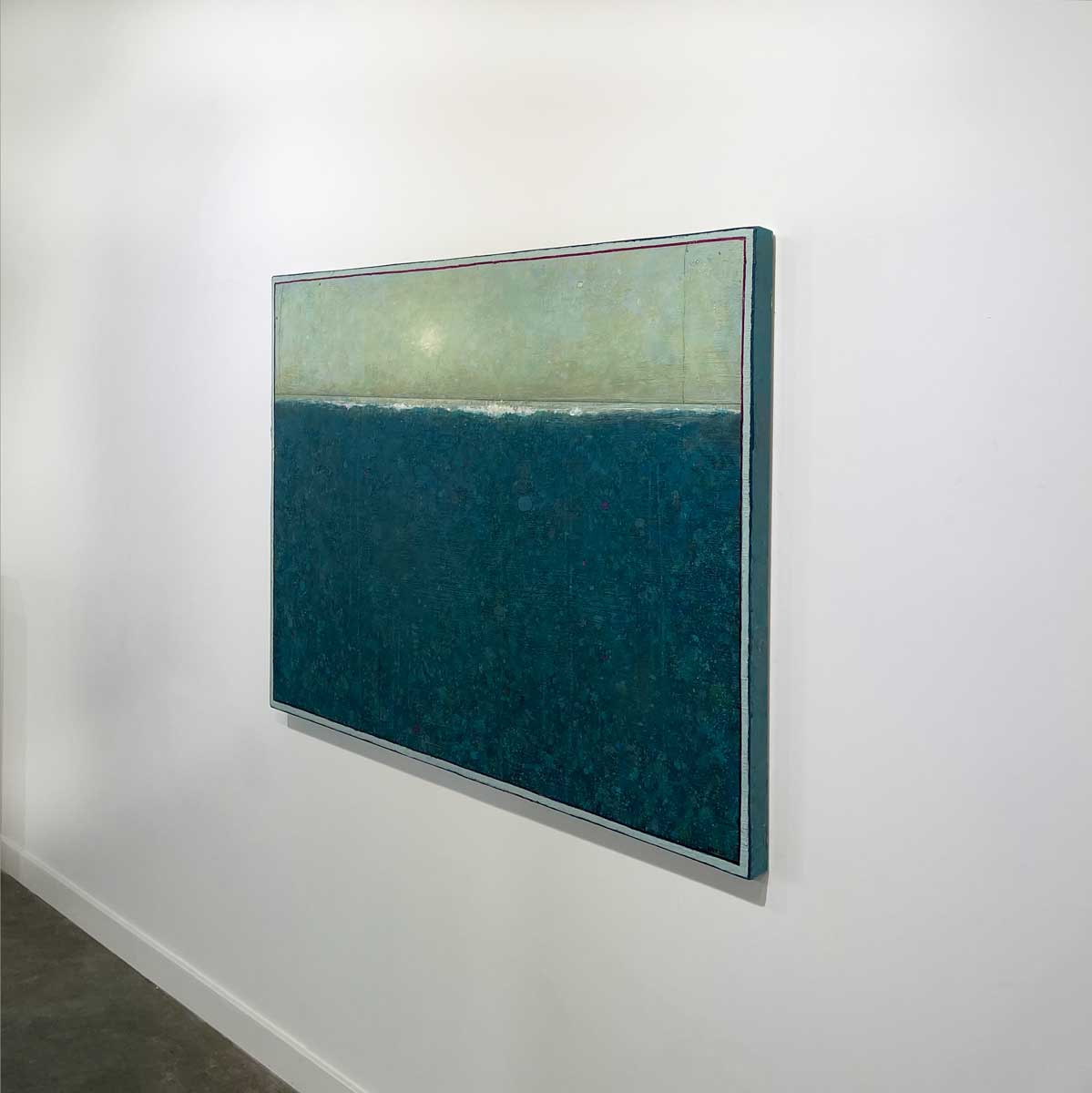 A right side-angle view of a blue and light green abstract landscape painting by Elwood Howell hangs on a white wall.