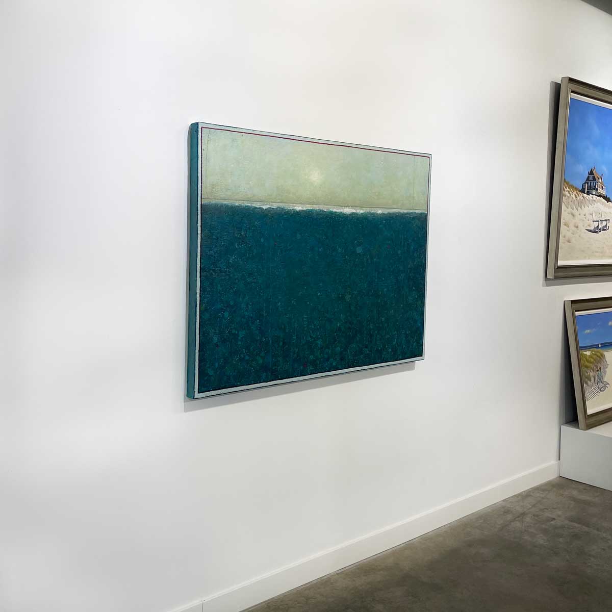 A left side-angle view of a blue and light green abstract landscape by Elwood Howell hangs on a white wall.