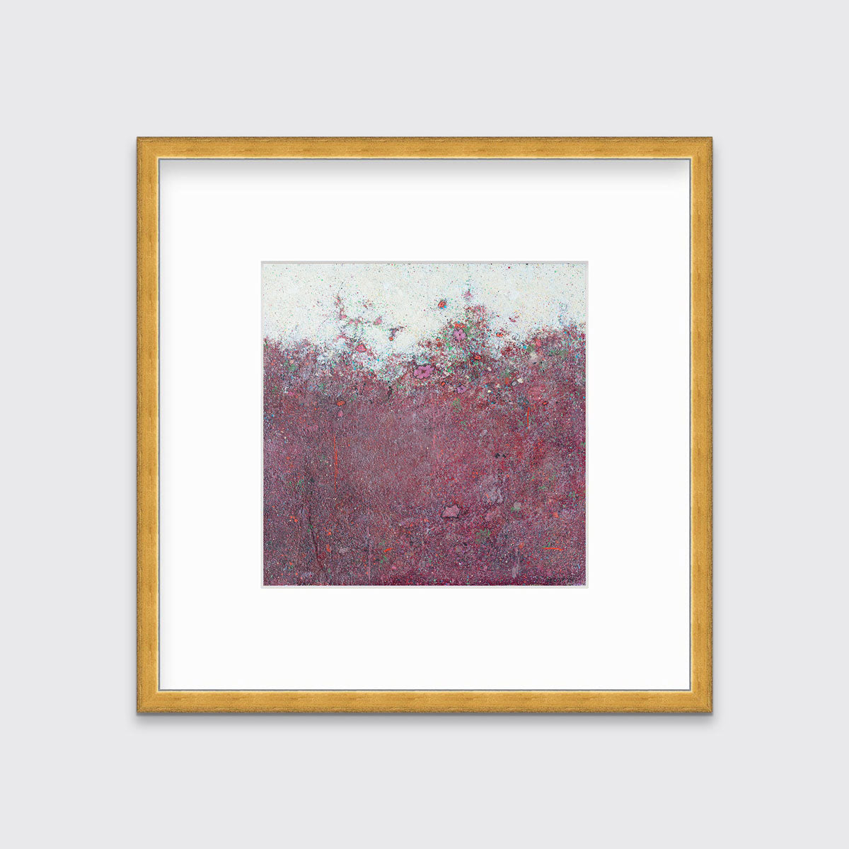 A dark red abstract landscape print in a gold frame with a mat hangs on a white wall.