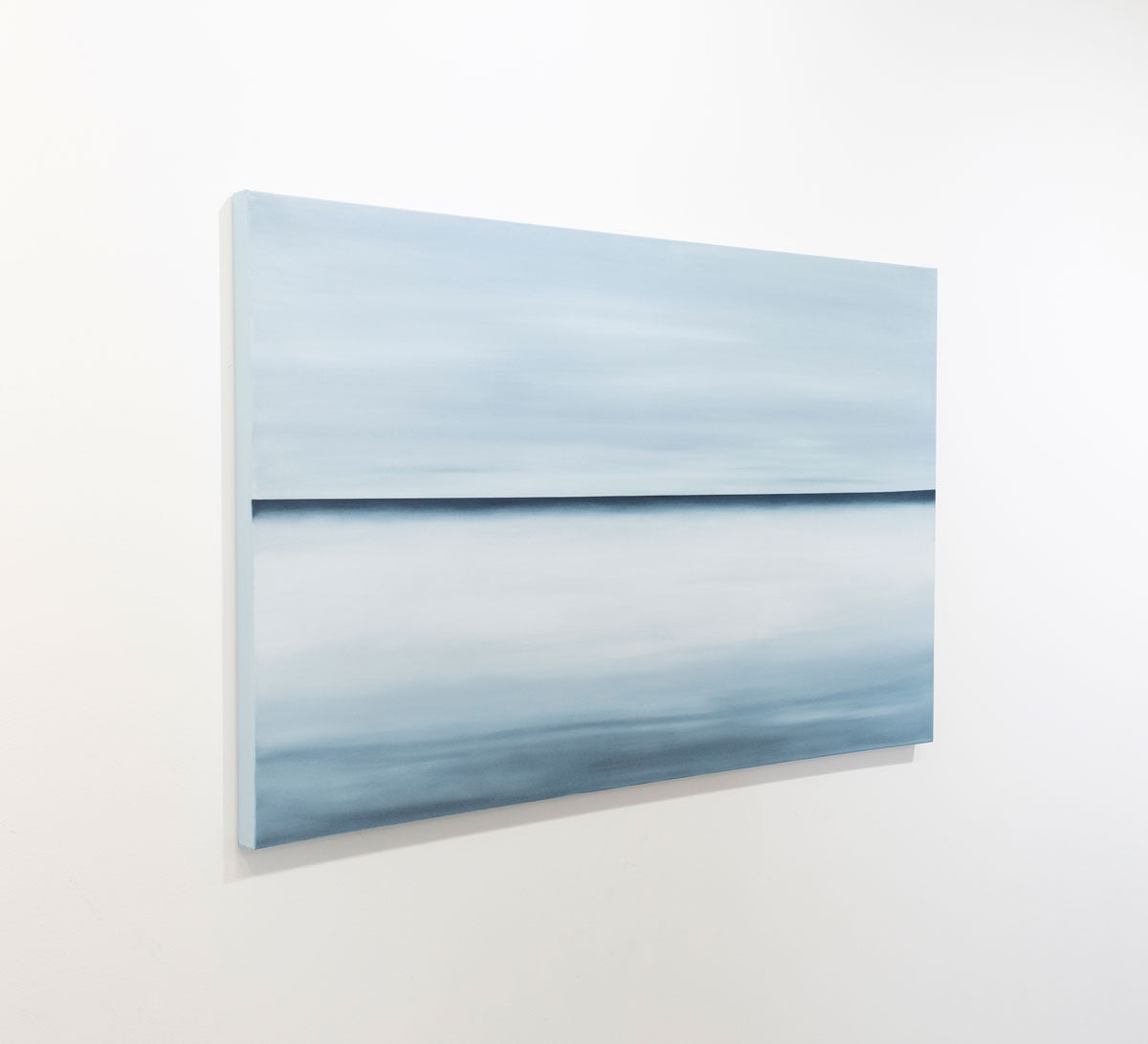 A blue oil painting with a single navy line in the middle of the canvas that suggests a horizon line is seen at an angle on a gallery wall. Wired and ready to hang.
