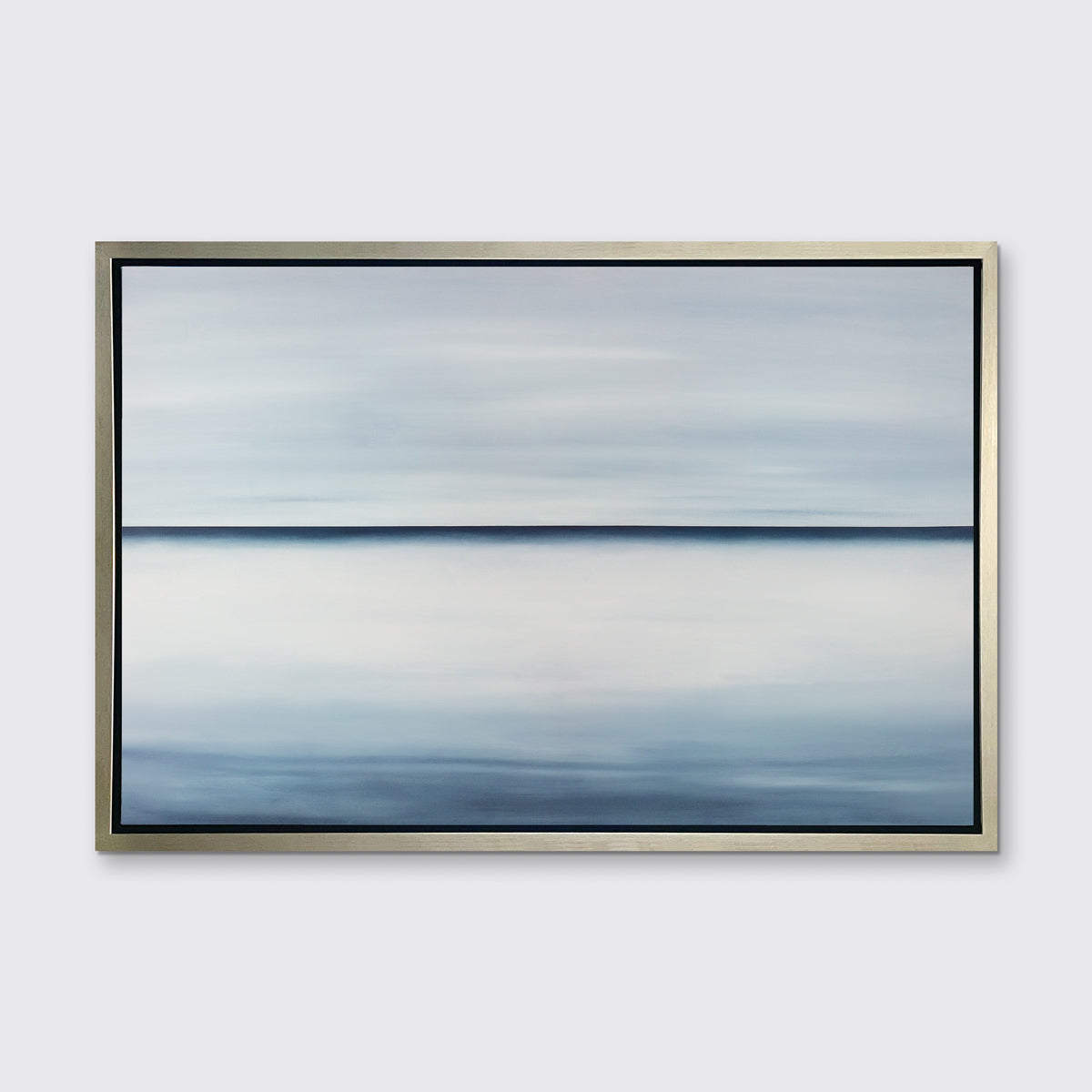A tonal blue abstract landscape print in a silver floater frame hangs on a white wall.