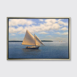 A blue, beige and white seascape print with sailboats in a silver floater frame hangs on a white wall.