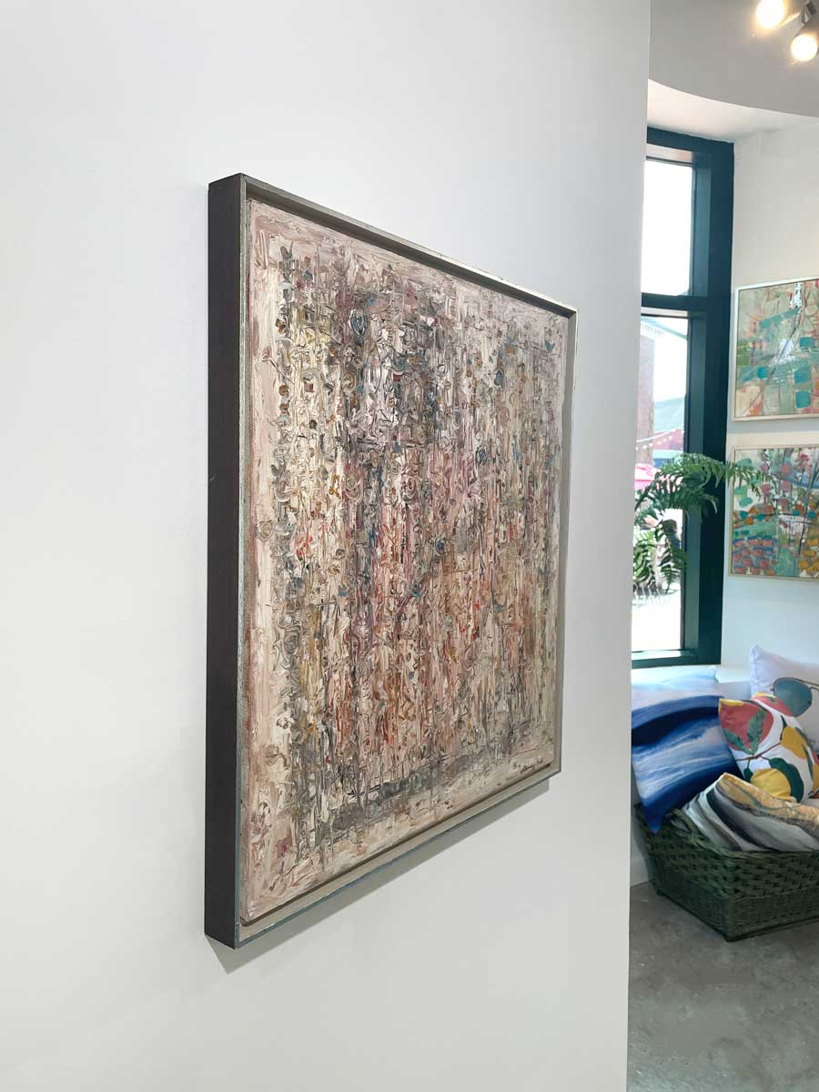 A left side-angle view of a white and multicolored abstract painting in a silver floater frame hangs on a white wall.